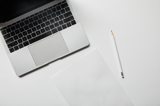 bovenaanzicht van laptop, papier en potlood op wit oppervlak - Foto, afbeelding