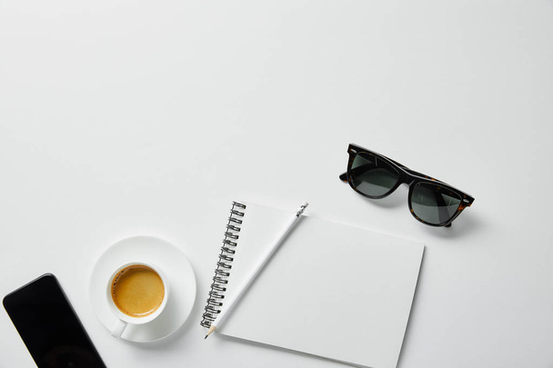 top view of coffee, notebook, pencil and glasses with smartphone on white surface - Foto, Imagen