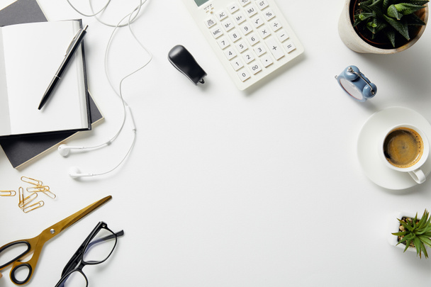 top view of plants, glasses, coffee, earphones and office supplies on white surface - Foto, imagen