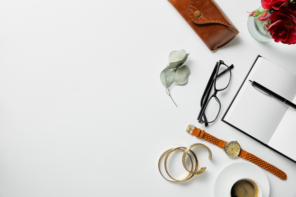 top view of jewelry, notepad, pen, glasses, case, plants and coffee on white surface - 写真・画像