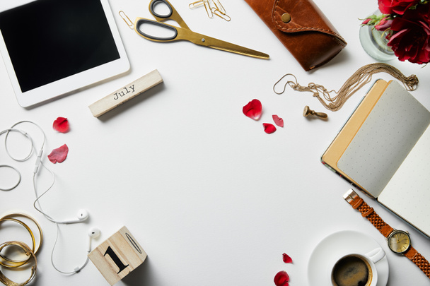 top view of digital tablet, jewelry, earphones, case, flowers, office supplies and coffee on white surface - Foto, imagen