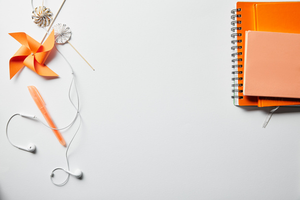 Draufsicht auf orangefarbene Notizbücher, Dekorationsgegenstände und Kopfhörer auf weißer Oberfläche - Foto, Bild