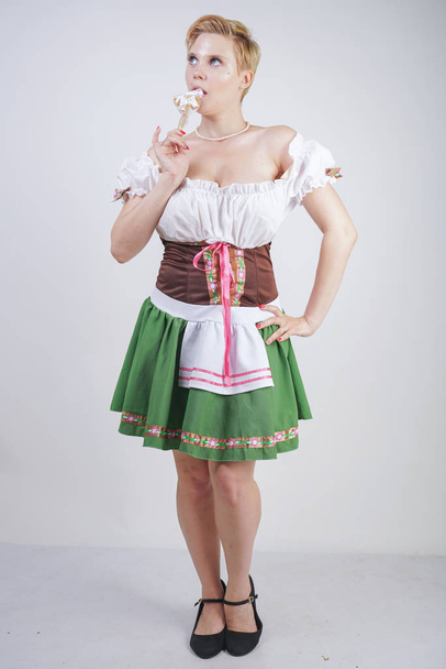 cute plus size girl with a short haircut and big Breasts dressed in a national Bavarian dress on a white background in the Studio. sexy curvy caucasian woman standing in cite dress with green skirt. - Fotoğraf, Görsel
