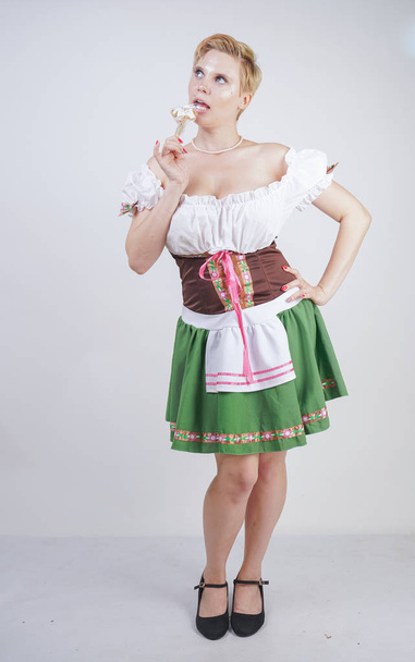cute plus size girl with a short haircut and big Breasts dressed in a national Bavarian dress on a white background in the Studio. sexy curvy caucasian woman standing in cite dress with green skirt. - Foto, afbeelding