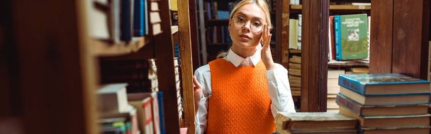 colpo panoramico di donna bionda in occhiali distogliendo lo sguardo in biblioteca
  - Foto, immagini