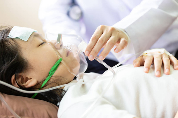 Closeup of hand female caregiver holding oxygen mask with cute child patient in hospital bed or home,little girl putting inhalation,doctor or nurse intensive care,health care,support,help concept - Valokuva, kuva