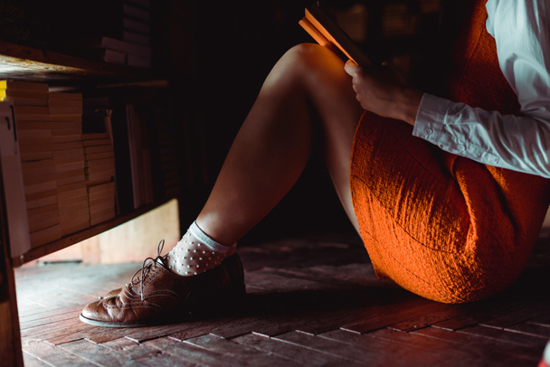 cropped view of woman sitting on wooden floor and holding book in library  - Foto, Imagem