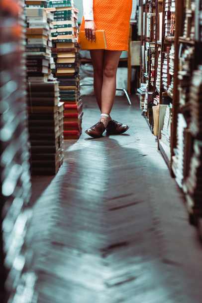 cropped view of woman holding orange book in library  - Foto, Bild