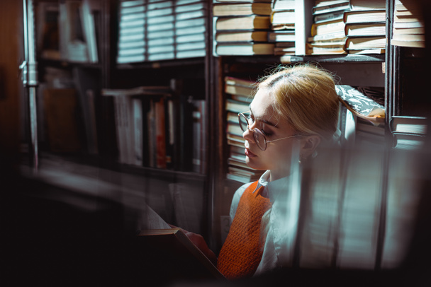 selective focus of beautiful and blonde woman reading book in library  - Zdjęcie, obraz
