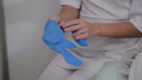 Ammattimainen kosmetologi käyttää sinisiä kumikäsineitä menettelyyn
. - Materiaali, video
