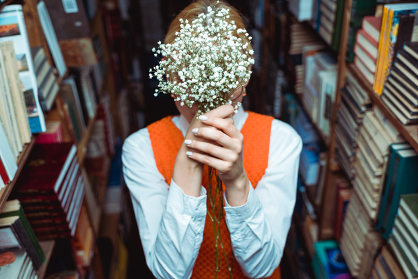 επιλεκτική εστίαση της γυναίκας που κρατά λευκά λουλούδια στη βιβλιοθήκη  - Φωτογραφία, εικόνα