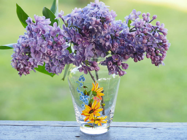 Tři větve lilaku ve skleněné váze stojí na okenní římse. Průhledná váza má vzorek žluté a modré barvy. Nádherná a jasná kytice květin může být skvělým dárkem pro někoho, kdo je tvou láskou nebo pro tvého partnera. - Fotografie, Obrázek