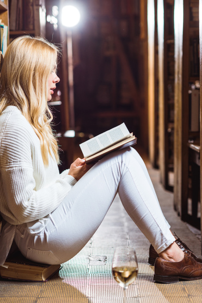 vue latérale du livre de lecture femme blonde et assis sur le sol dans la bibliothèque
  - Photo, image