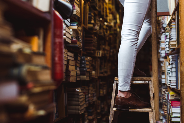 selectieve focus van vrouw staande op houten ladder in bibliotheek  - Foto, afbeelding