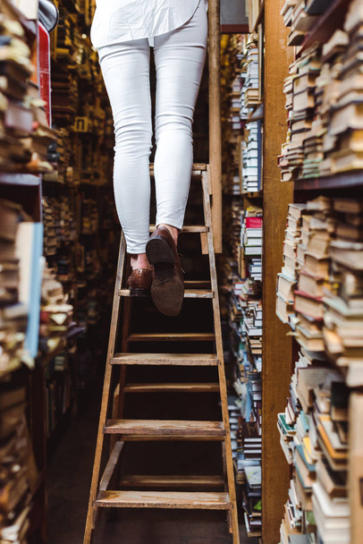 cropped view of woman standing on wooden ladder in library  - Photo, Image