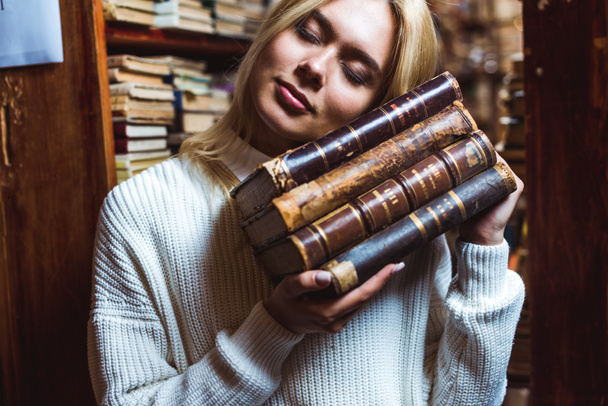 blonde and pretty woman with closed eyes holding books in library  - Photo, Image