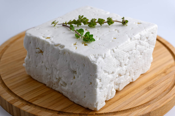 Grande pezzo di tradizionale formaggio greco feta su tagliere in legno con origano su sfondo bianco
 - Foto, immagini