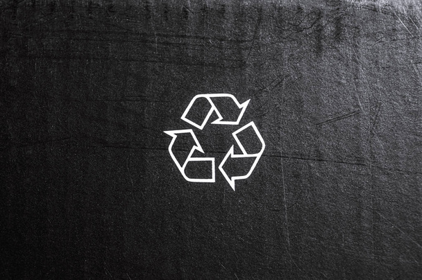 Fekete textúrájú kartondoboz háttere nyomtatott fehér újrahasznosítási logo jellel. Szóköz a szöveghez. Minimalista stílusú sablont. Vízszintes képernyőtájolás - Fotó, kép