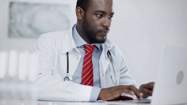 koncentrált afro-amerikai orvos használ laptop, miközben ül a munkahelyen laboratóriumi - Felvétel, videó