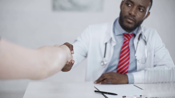 nyájas afro-amerikai orvos kezet, miközben beteg ül a munkahelyen a kórházban - Felvétel, videó