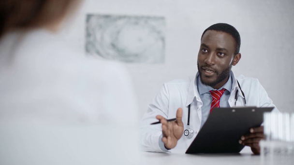 positive african american doctor talking with colleague while looking at clipboard with diagnosis - Footage, Video