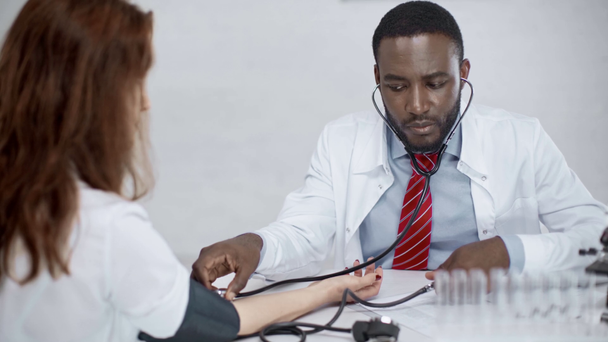 attente Afro-Amerikaanse arts die geduldig onderzoekt met stethoscoop op de werkplek in het ziekenhuis - Video