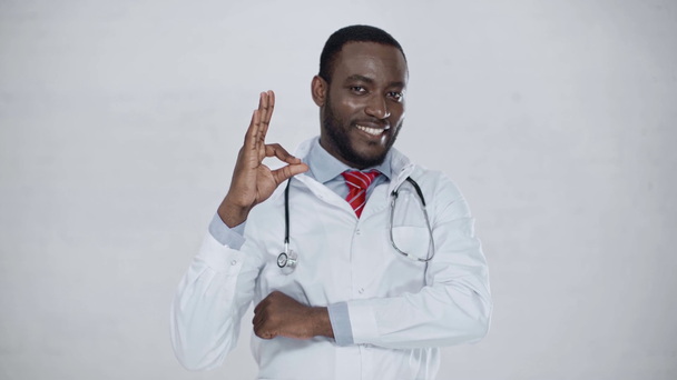 fröhlicher afrikanisch-amerikanischer Arzt, der mit verschränkten Armen dasteht, Ok-Zeichen zeigt und in die Kamera lächelt - Filmmaterial, Video
