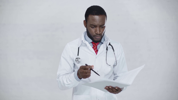 уважний афроамериканський лікар, дивлячись на папери в папці, посміхаючись і дивлячись на камеру
 - Кадри, відео