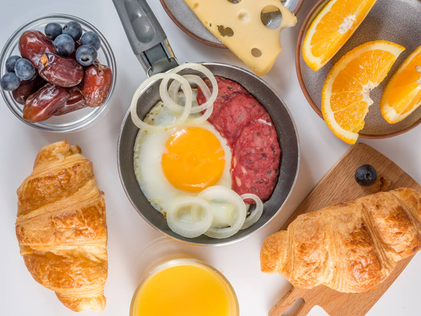 Vue de dessus d'un petit déjeuner continental avec croissants et oeufs frits et jus d'orange et café et fromage sur fond blanc
. - Photo, image