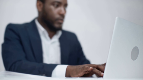selective focus of concentrated african american businessman using laptop while sitting at workplace in office - Metraje, vídeo