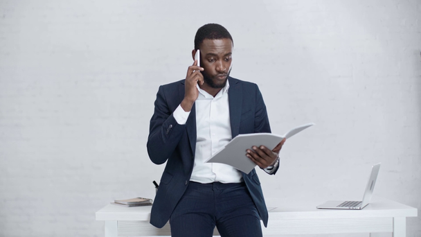 σοβαρός Αφρικανός Αμερικανός επιχειρηματίας που μιλά στο smartphone ενώ στέκεται στο χώρο εργασίας - Πλάνα, βίντεο