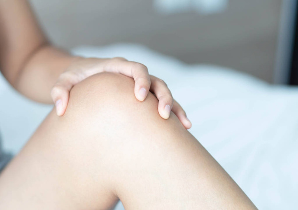 Detailní žena ruka drží koleno s bolestí na posteli, zdravotní péče a lékařské koncepce - Fotografie, Obrázek