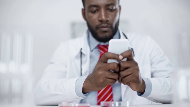 selektiver Fokus afrikanisch-amerikanischer Wissenschaftler mit Smartphone im klinischen Labor - Filmmaterial, Video