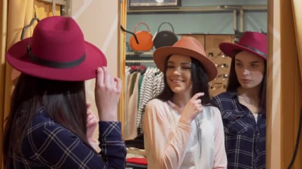 Twee jonge mooie vrouwen die op hoeden proberen, terwijl ze samen winkelen - Video
