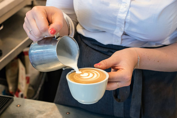 Female barista pouring hot milk on a cup to make art cappuccino. - Foto, immagini