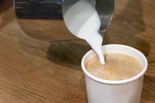 Gieten van hete schuim melk op een plastic beker voor een take-away koffie. - Foto, afbeelding