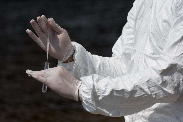 Teilansicht des Wasserinspektors in Latexhandschuhen mit Reagenzglas zur Entnahme einer Wasserprobe - Foto, Bild