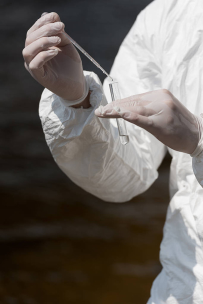 Vista parcial del inspector de agua en guantes de látex con tubo de ensayo tomando muestra de agua
 - Foto, Imagen