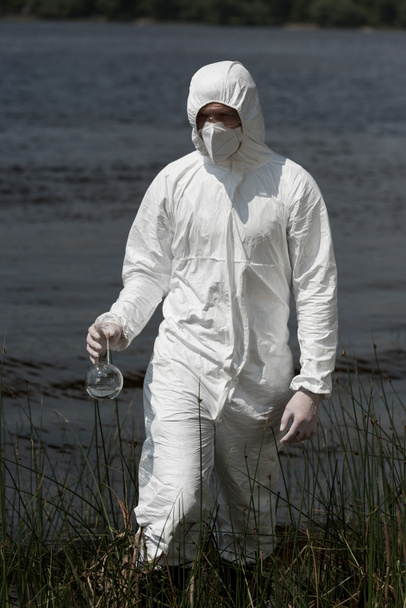 water inspecteur in beschermend kostuum, ademhalingsmasker en bril houder met watermonster - Foto, afbeelding