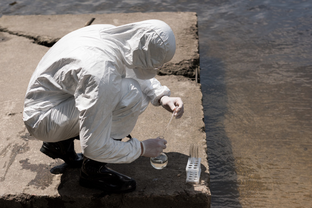 Inspektor wody w stroju ochronnym, rękawice lateksowe i respirator biorąc próbki wody na rzece - Zdjęcie, obraz