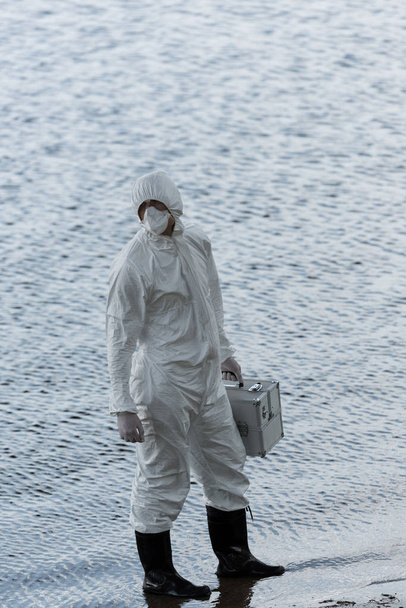 full length view of water inspector in protective costume holding inspection kit at river - Photo, Image