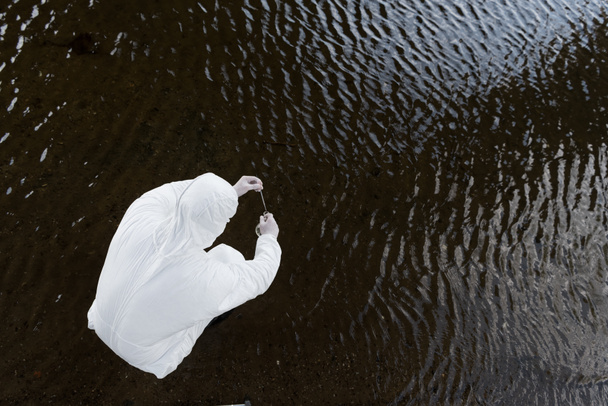 верхний вид водного инспектора в защитном костюме, берущего образец воды из реки
 - Фото, изображение