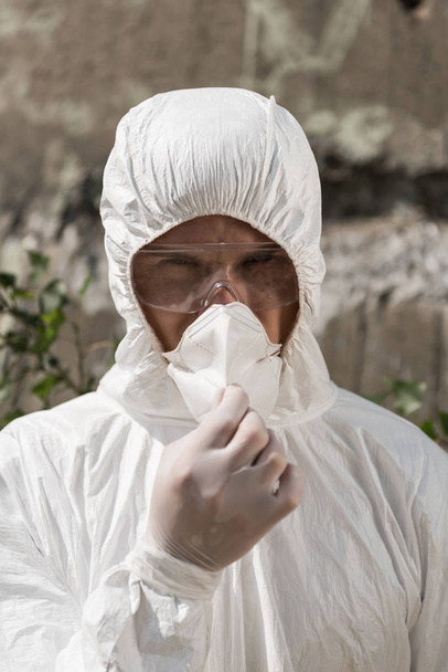 front view of ecologist in protective costume and goggles taking off respirator - Photo, Image