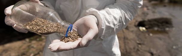 panoramic shot of ecologist in latex gloves holding bottle with pebbles - Foto, Bild