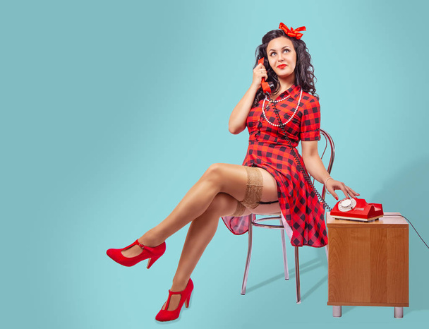 happy young pinup woman sitting on a chair and talking on phone - Photo, Image