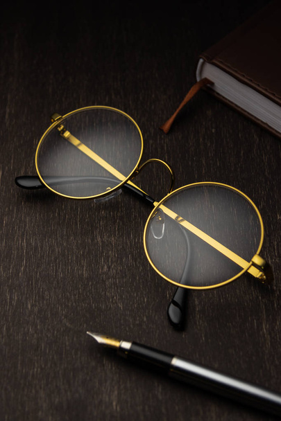 gold glasses, pen on a dark wooden background - Fotoğraf, Görsel
