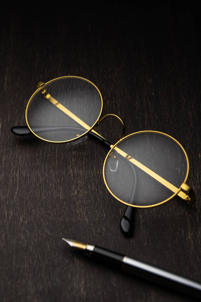 gold glasses, pen on a dark wooden background - Fotoğraf, Görsel