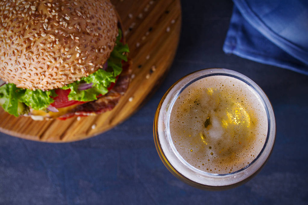 Beer and burger on wooden board for serving. Beer and food concept - Image - Fotó, kép