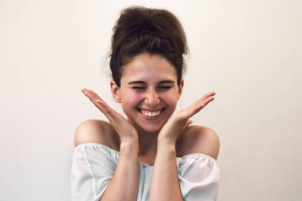 Close up photo portrait of young beautiful woman with freckles which happy and screams for joy. She is positively surprised and holds palms near her face. Funny face on gray background - Photo, image