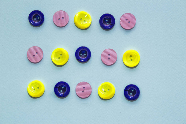 青い背景に様々な多色の縫製ボタンのコレクション。黄色、紫、濃い青色のボタン。ミニマリズム。縫製アクセサリー。フラットレイ、テキスト用の場所 - 写真・画像